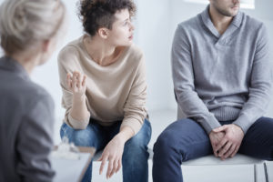 Married couple fighting in couples counseling and looking upset about the tone of communication in their marriage. Wife is holding hand and trying to talk while husband is closed off and looks away. Couples therapy in Fairfax, VA can help you communicate more respectfully. Marriage counseling in Fairfax, VA can help improve the communication in your marriage at The Center for Connection, Healing and Change. 22032